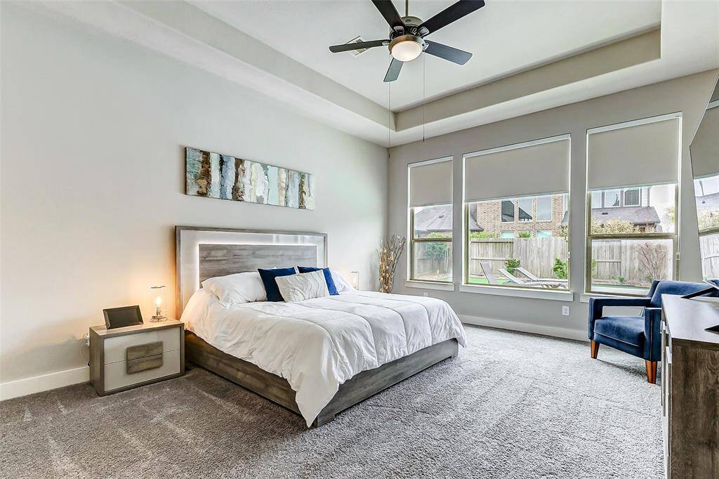 Primary bedroom features a modern design with ceiling fan and vaulted ceiling. Ample natural light fills the room through multiple windows overlooking a beautiful pool. Cozy carpeting and neutral tones create a serene atmosphere.