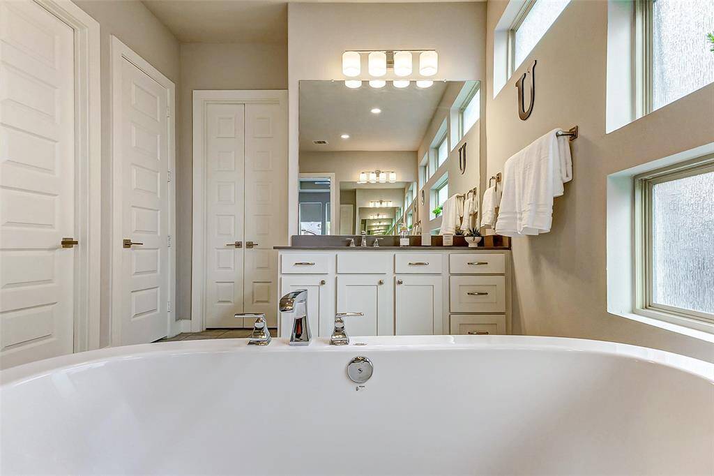This bathroom features a modern design with a large soaking tub, dual sinks with ample counter space, and sleek cabinetry. Plenty of natural light streams through frosted windows, creating a bright and inviting atmosphere.