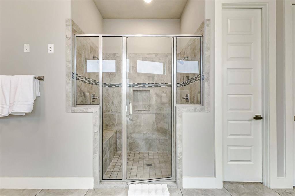 This modern bathroom features a spacious, glass-enclosed shower with 2 shower heads, stylish tile work and a built-in bench.