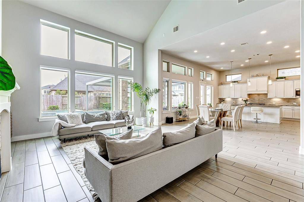 Open-concept living area features high ceilings and large windows for abundant natural light. It seamlessly connects the modern kitchen, dining, and living spaces, creating an inviting atmosphere ideal for entertaining and family gatherings.