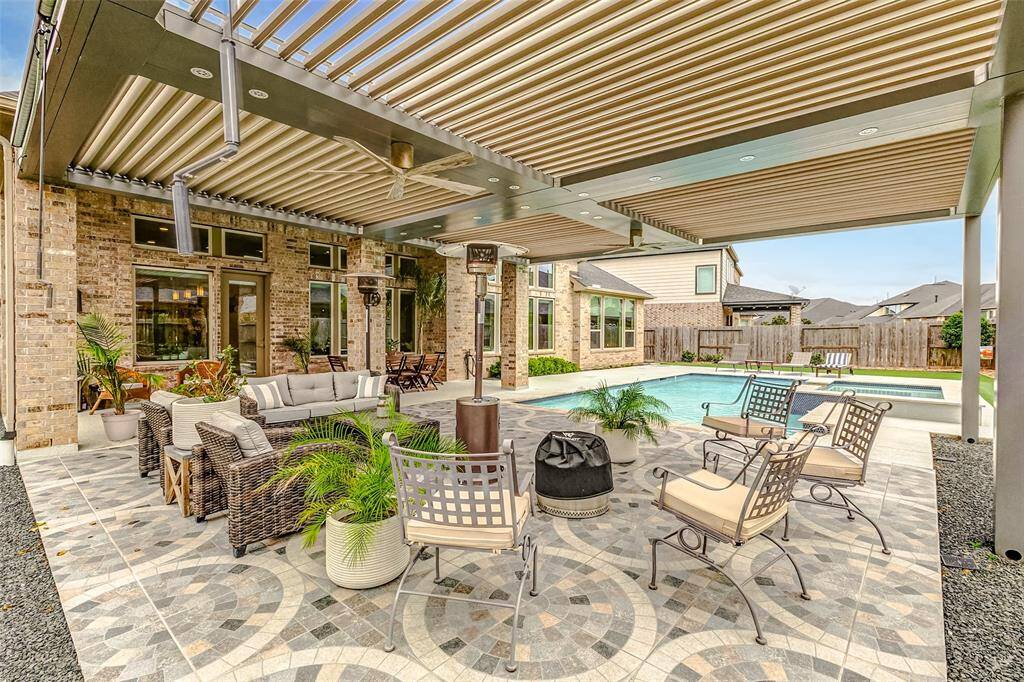 This photo showcases a spacious outdoor patio with stylish furniture, a modern pergola, and a well-maintained pool. The area features decorative tile flooring and lush greenery, creating an inviting space for relaxation and entertainment.