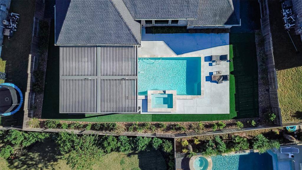 Modern backyard featuring a sleek swimming pool with a hot tub, surrounded by a spacious concrete patio. Adjacent to the house, there's a covered area and green lawn.