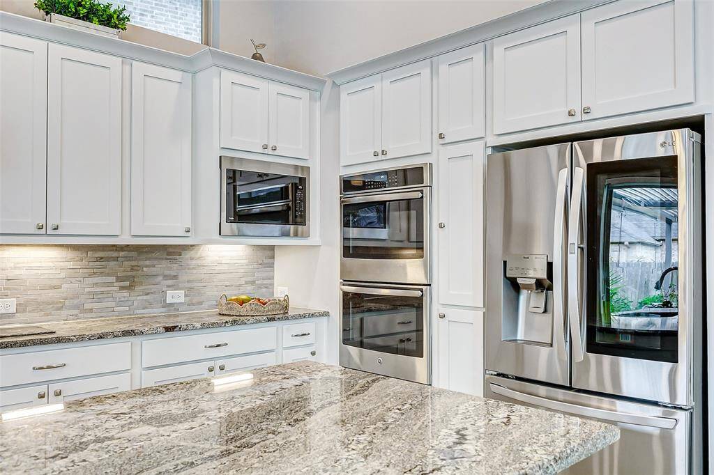 This modern kitchen features sleek stainless steel appliances, including a double oven. The space is enhanced by white cabinetry, granite countertops, and a stylish tile backsplash, creating a bright and contemporary atmosphere.