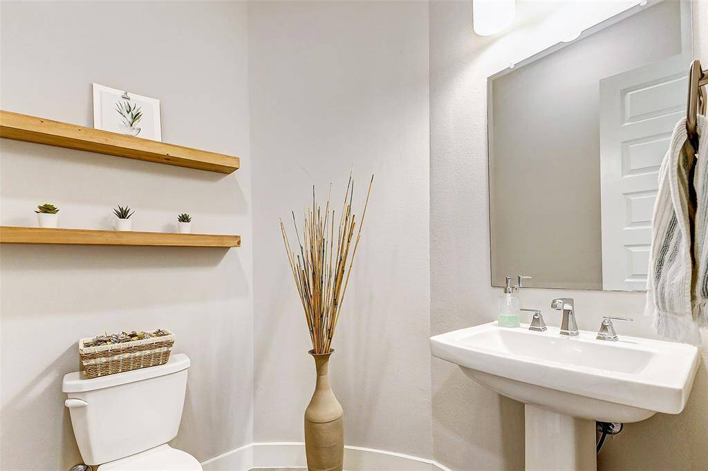 Modern, minimalist half bathroom with a pedestal sink, a large mirror, and a clean, neutral color palette. It features wooden floating shelves adding a touch of nature and warmth.