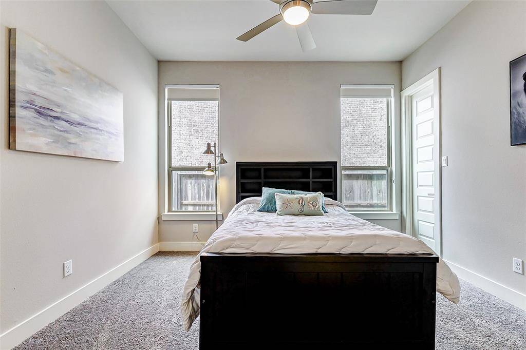 Cozy layout  two large windows providing natural light, neutral walls, and modern decor. A ceiling fan adds comfort, and plush carpeting enhances the warmth of the space.
