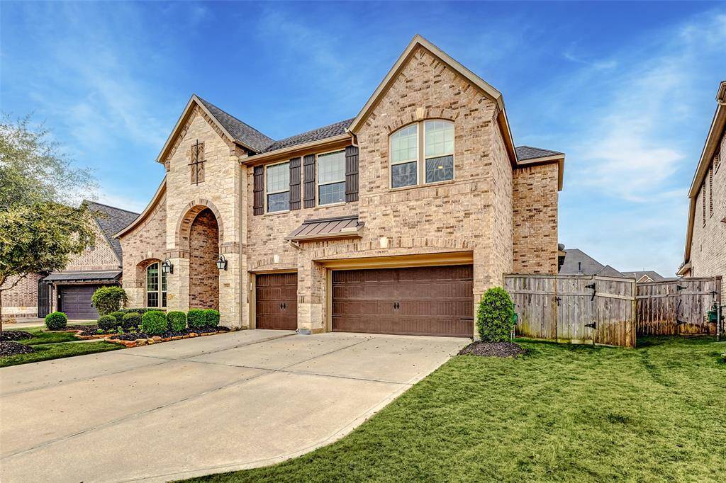 Spacious two-story brick home with a three-car garage. It features a well-maintained lawn and landscaped front yard, along with a wooden fence for privacy. The exterior has a classic, inviting look with arched entryways and large windows.