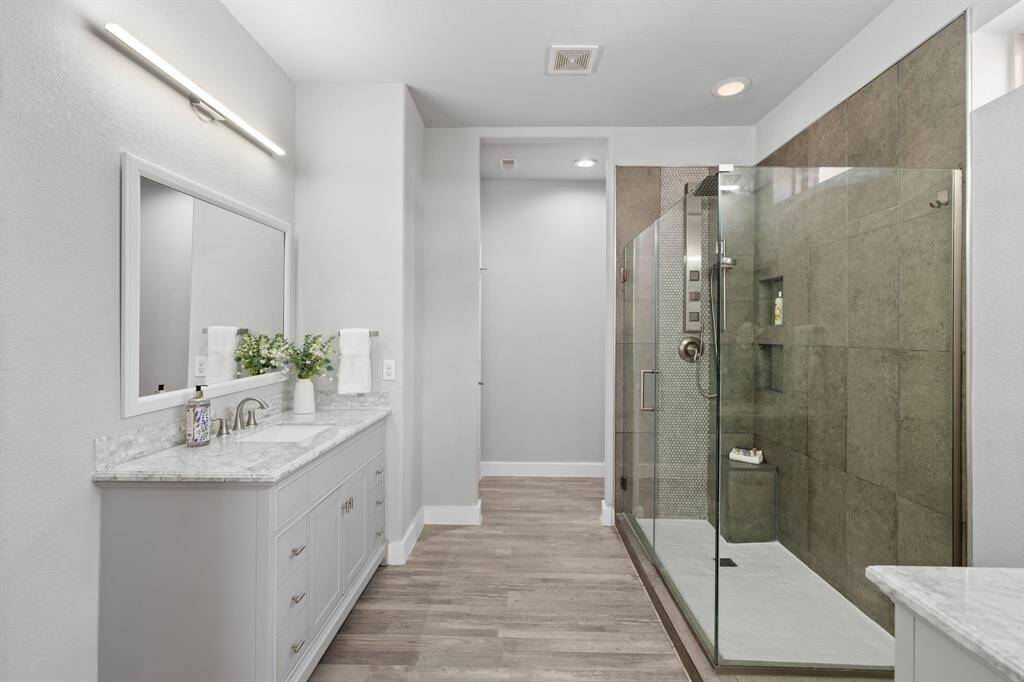 UPDATED modern bathroom features a spacious glass-enclosed shower with sleek tilework, a large vanity with ample storage, and elegant finishes. The neutral color palette and natural light create a bright, inviting space.