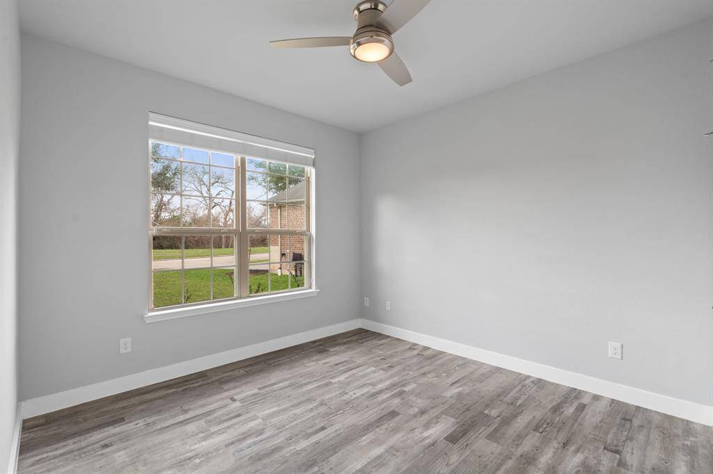 The secondary/guest bedroom is conveniently located at the front of the home to the left, offering privacy for guests. This inviting space features soft gray walls, stylish wood-look flooring, and a large window that fills the room with natural light and scenic outdoor views. A ceiling fan enhances comfort, making it a perfect retreat.