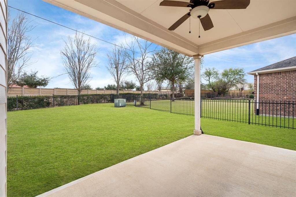 Spacious backyard with a covered patio featuring a ceiling fan. The area is partially fenced, providing privacy and security, offers ample space for outdoor activities.