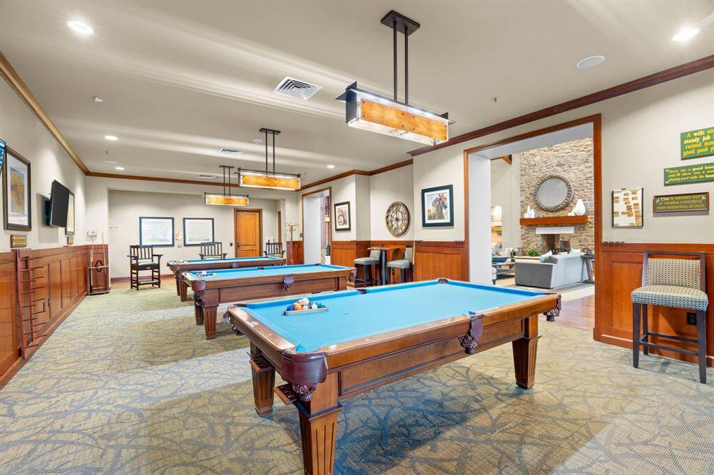 This spacious recreation room features two billiards tables, elegant lighting, and cozy seating areas. It opens into a living area with a stone fireplace, offering a perfect blend of entertainment and relaxation.