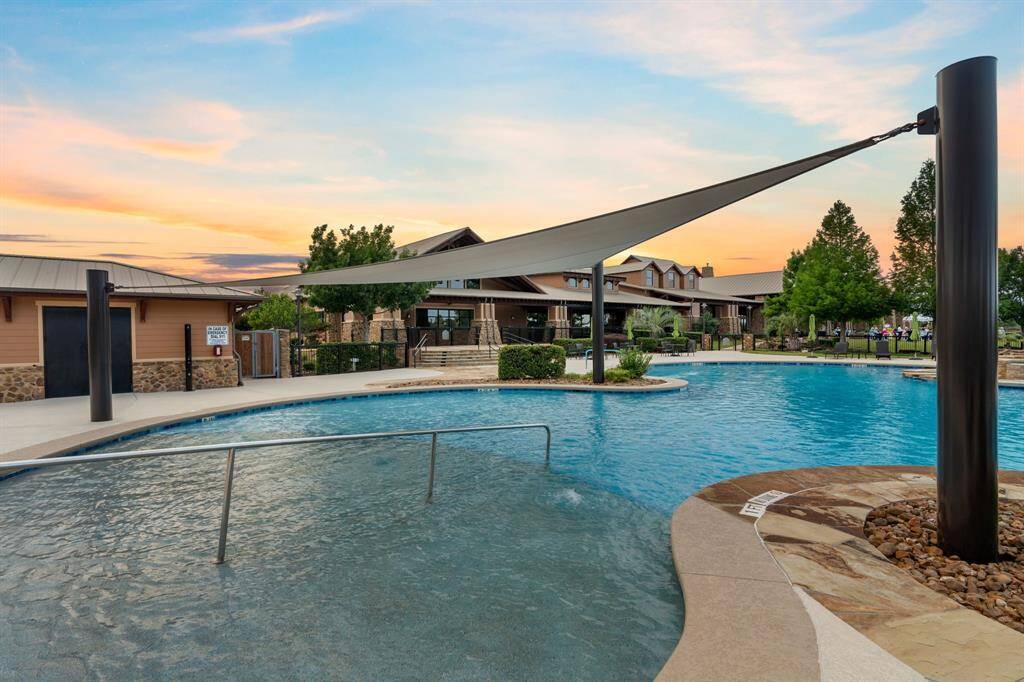 Beautifully landscaped community pool area with a modern shade sail, surrounded by greenery and a clubhouse. Ideal for relaxation and social gatherings.