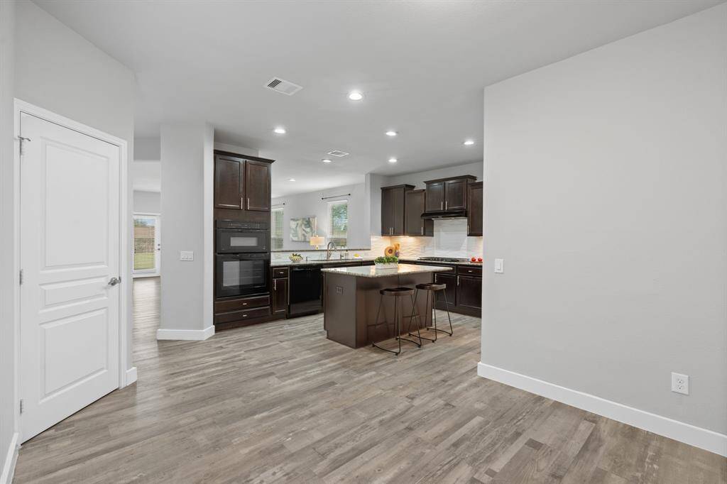 This modern kitchen features dark wood cabinetry, sleek black appliances, and gleaming granite countertops, with a spacious island perfect for baking bread or cookies. Additional seating at the island provides extra space for guests to gather. The appliances have been gently used and remain in excellent condition, adding to the kitchen's appeal.