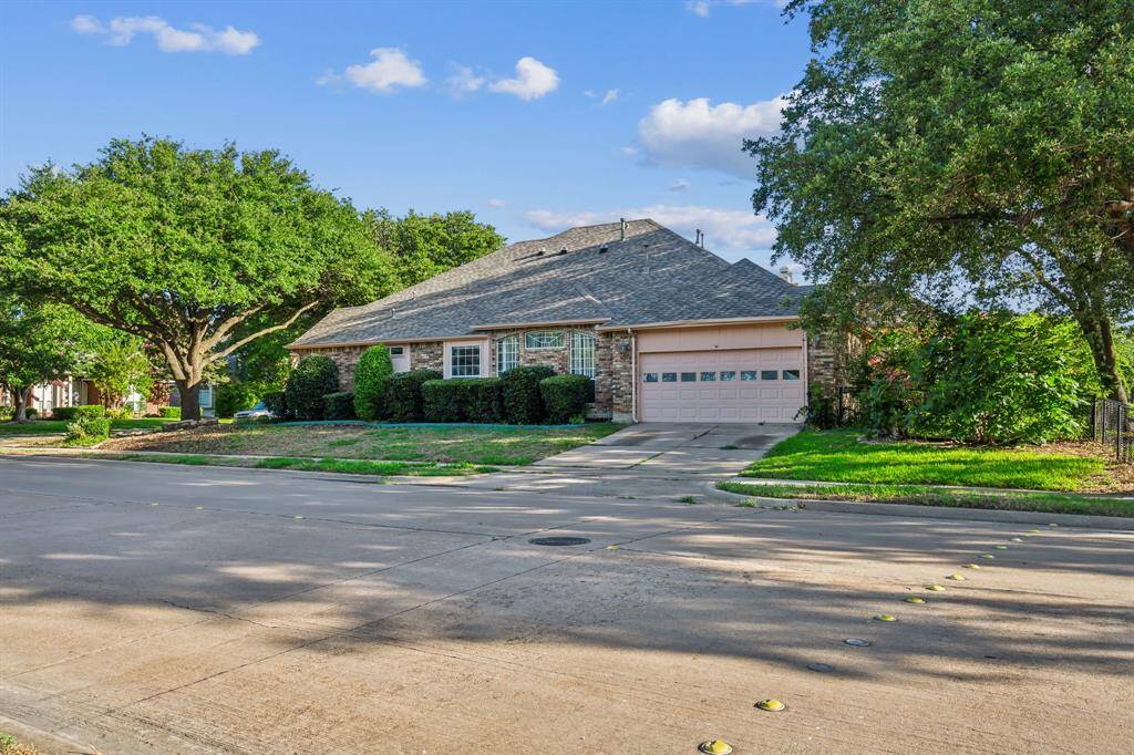 This photo shows a charming single-story brick home with a well-maintained lawn and mature trees. The house features a double garage and a sloped roof, situated in a quiet neighborhood.