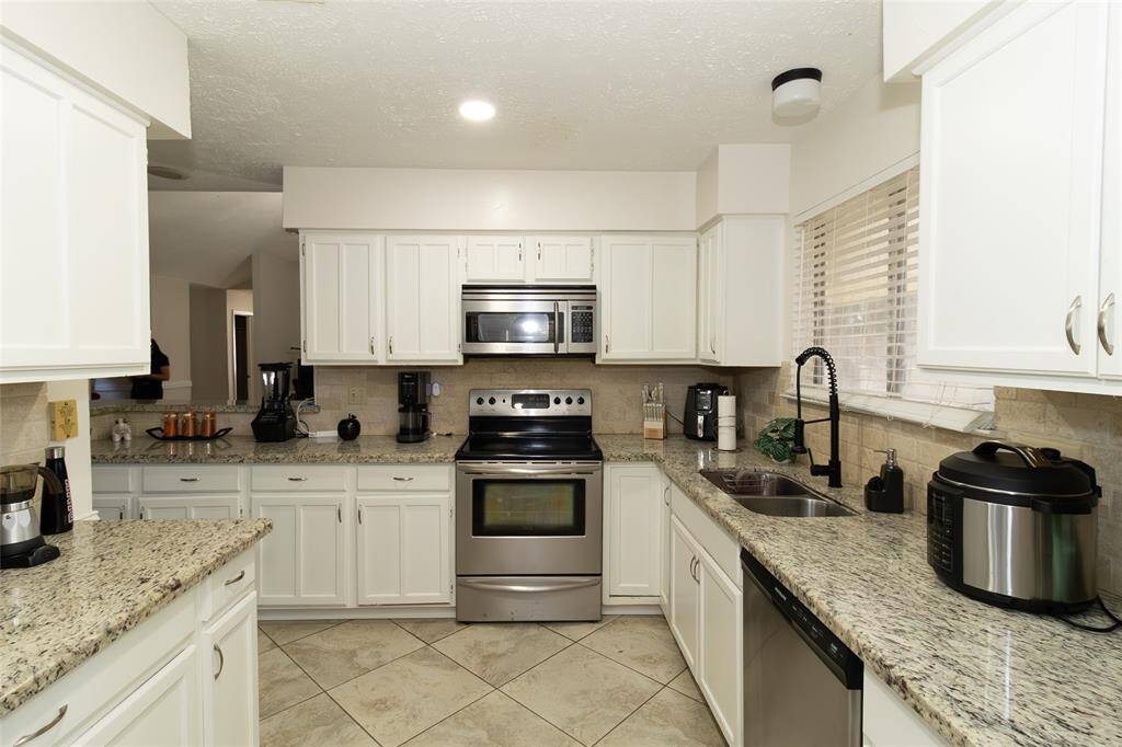 This kitchen features modern stainless steel appliances, granite countertops, and ample white cabinetry. The open layout provides plenty of workspace, with a double sink and stylish fixtures. Natural light enters through a window, brightening the space.
