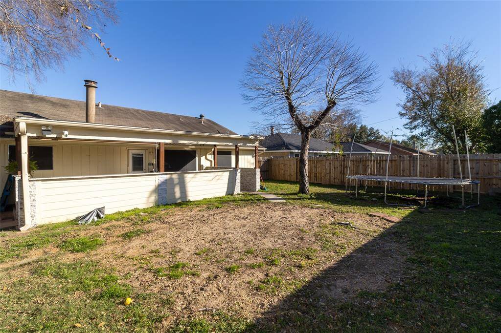 This photo shows a backyard with a covered patio, a wooden fence, and a mature tree. The yard offering ample space for outdoor activities.