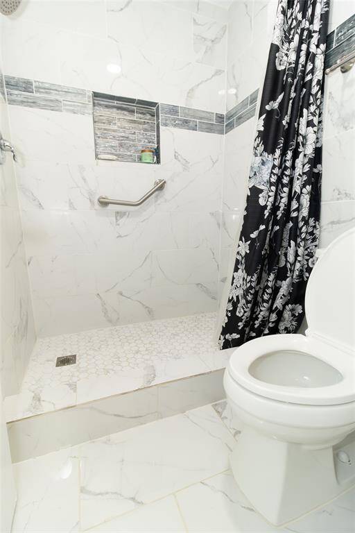 This bathroom features a modern design with marble-patterned tiles, a walk-in shower with a decorative tile accent.