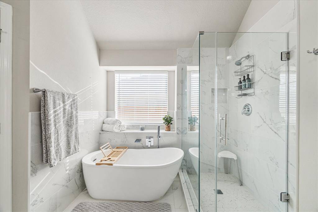Experience luxury in the updated primary bath, featuring a serene soaking tub, a sleek glass-enclosed shower, and abundant natural light.
