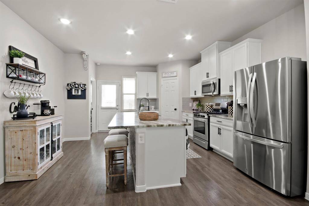This kitchen features a modern design with stainless steel appliances, white cabinetry, and a large central island with seating. The space is well-lit with recessed lighting and has a clean, open layout perfect for cooking and entertaining.