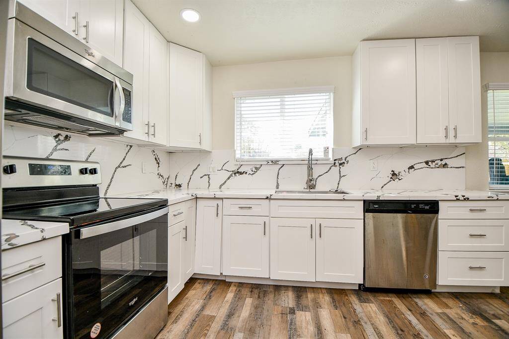 This kitchen area is complete with recessed lighting, laminate wood floors, stainless steel appliances, and plenty of cabinets for storage.