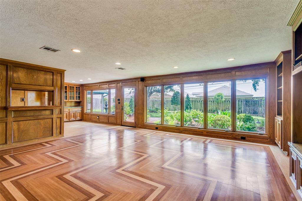 Spacious family room with herringbone vinyl plank flooring, built-in wooden cabinetry, and large windows offers ample natural light and a view of a lush backyard.