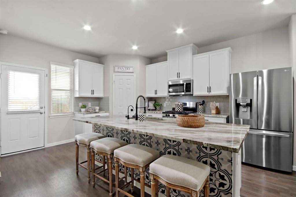 Another view of a large island with stylish custom mosaic tiling. So many beautiful finishing touches. The space is bright with recessed lighting and includes a pantry and ample seating, perfect for family gatherings. To the left there's a door to the spacious backyard.