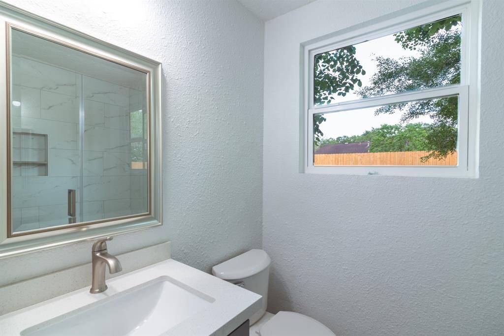 Bright, modern kitchen with stainless steel appliances, white cabinetry, and sleek countertops. Features a large fridge, oven, microwave, and a spacious sink area, all complemented by wood-style flooring and ample natural light.