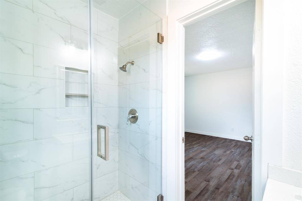 Bright kitchen with large windows overlooking a fenced backyard. Features modern stainless steel appliances, white cabinetry, and dark wood flooring.