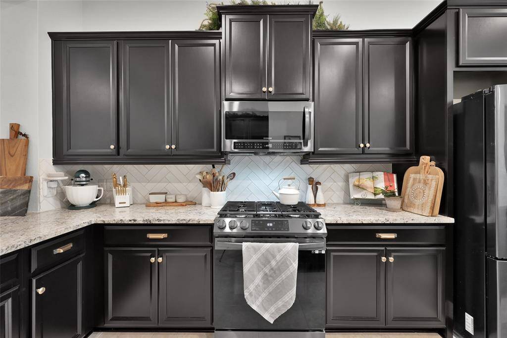Modern kitchen with abundant sleek blackcabinetry, stainless steelappliances, granite countertops,and herringbone tile backsplash.