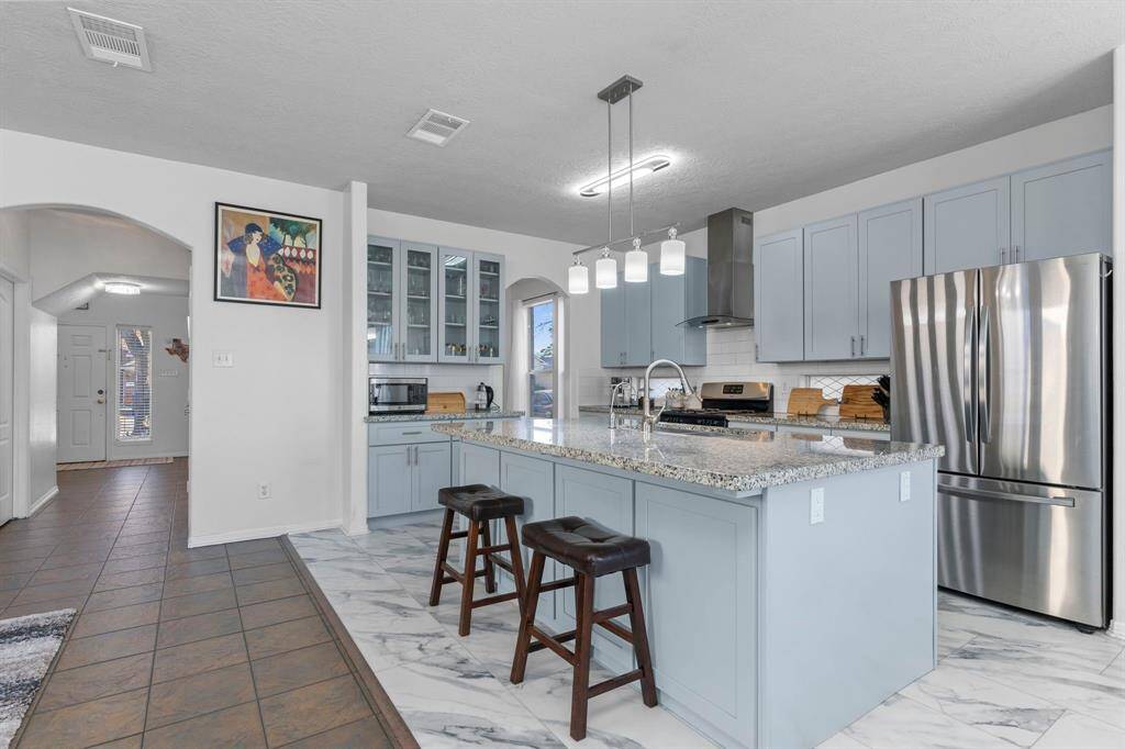 Renovated kitchen featuring brand-new cabinets, hardware, light fixtures, backsplash, island, vent hood, sink, granite countertops, refrigerator, dishwasher, and flooring—all updated in 2023!