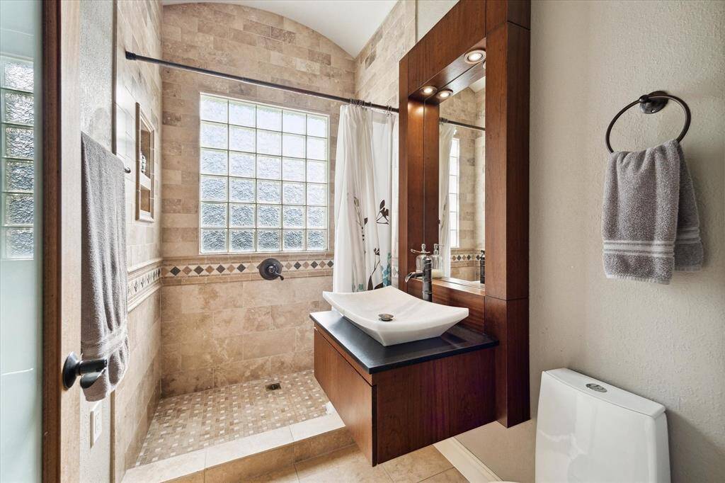 In the large bathroom, glass brick and floor-to-ceiling tile surround a walk-in shower, two-stage commode and custom floating vanity.