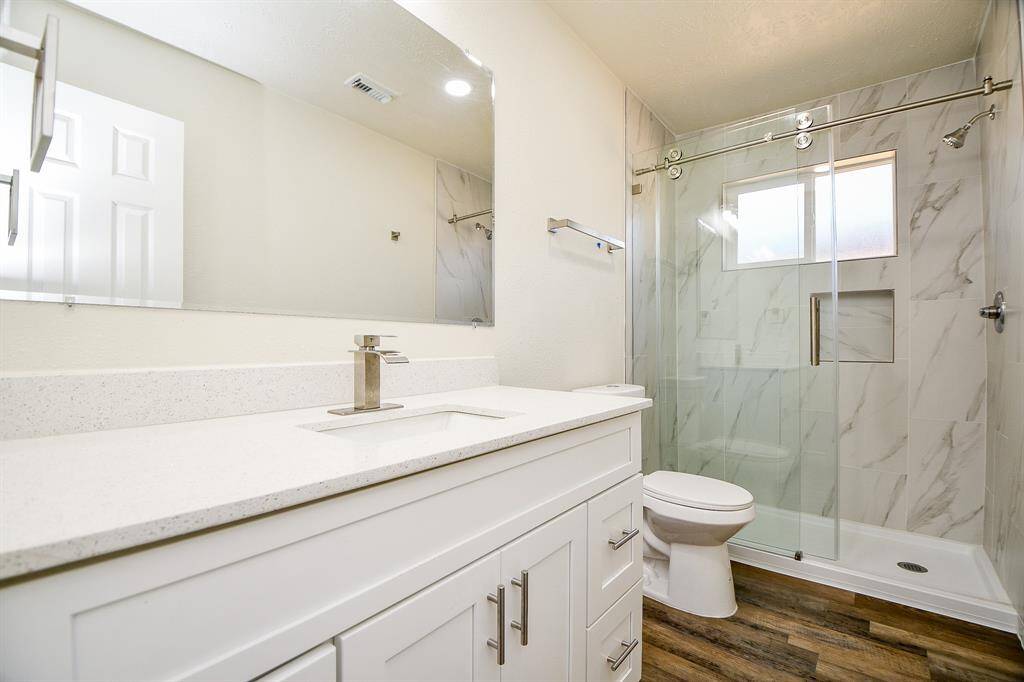 This stunning bathroom features laminate wood floors, granite countertops and backsplash, plenty of wooden cabinetry, a large mirror, and recessed lighting.