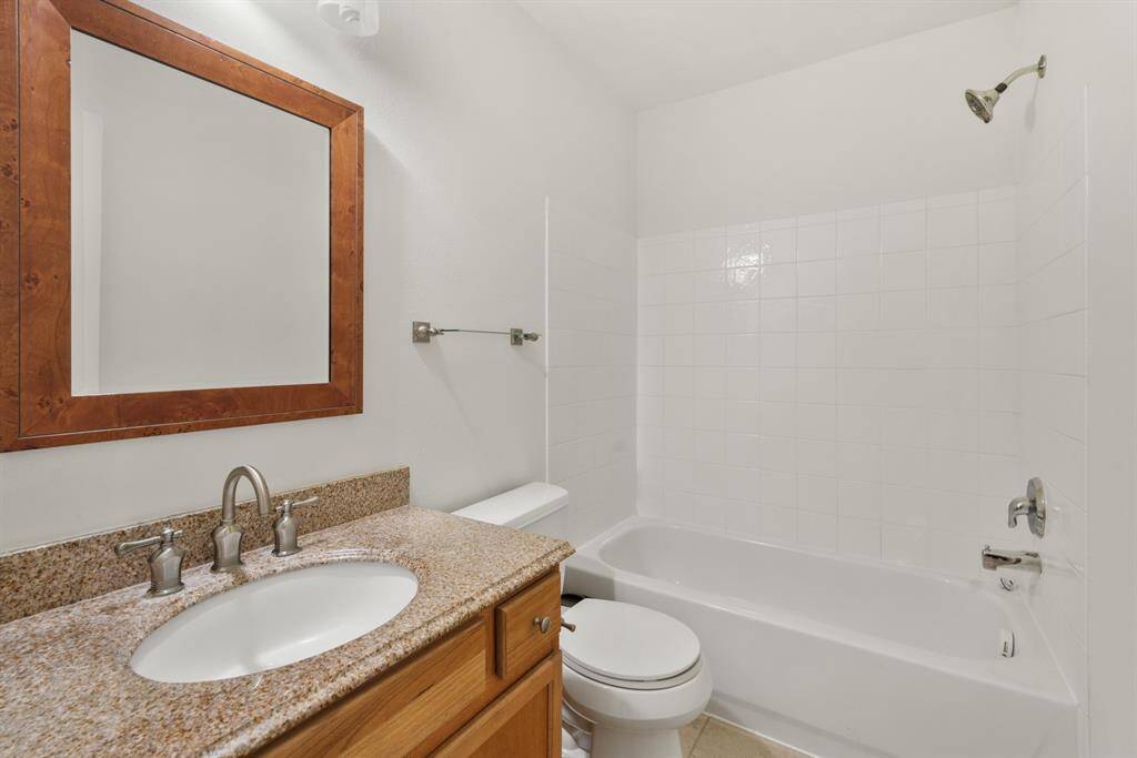 Secondary Bathroom, featuring tile flooring, shower/tub combo with a tile shower wall, wood cabinets and granite countertops, and a framed mirror.