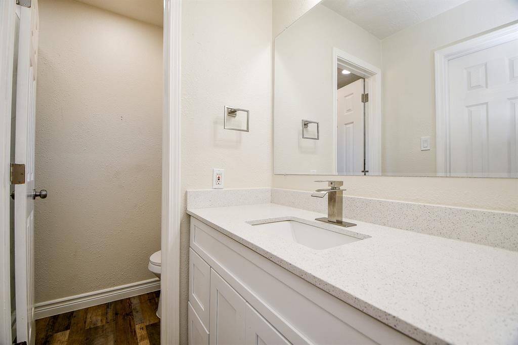 This stunning bathroom features laminate wood floors, granite countertops and backsplash, plenty of wooden cabinetry, and a large mirror.
