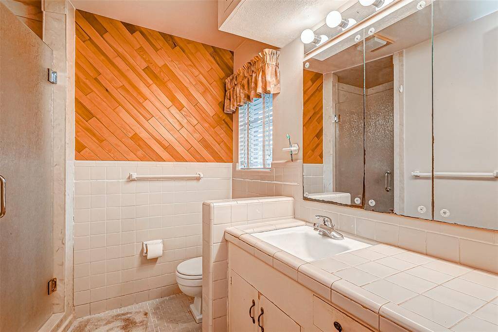 This primary bath, conveniently attached to the primary bedroom, offers a blend of character and functionality. A unique wood accent wall adds warmth and texture, creating a cozy and inviting atmosphere.