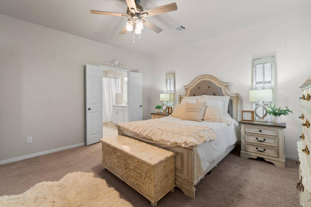This cozy primary bedroom features a plush carpet, beautiful natural light, & spacious enough for heavy wooden furniture. A ceiling fan (with remote) adds comfort, and double doors open to the ensuite bathroom, enhancing convenience and comfort.