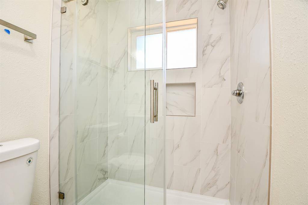 Highlighting an amazing glass enclosed shower with gorgeous tile, and a window that lets in natural light.