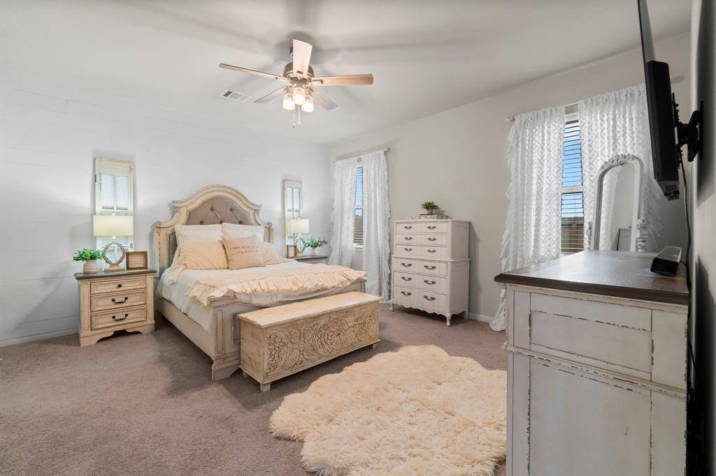 This primary bedroom boasts neutral tones with a shiplap accent wall, has two large windows, creating a bright, warm, & inviting atmosphere.