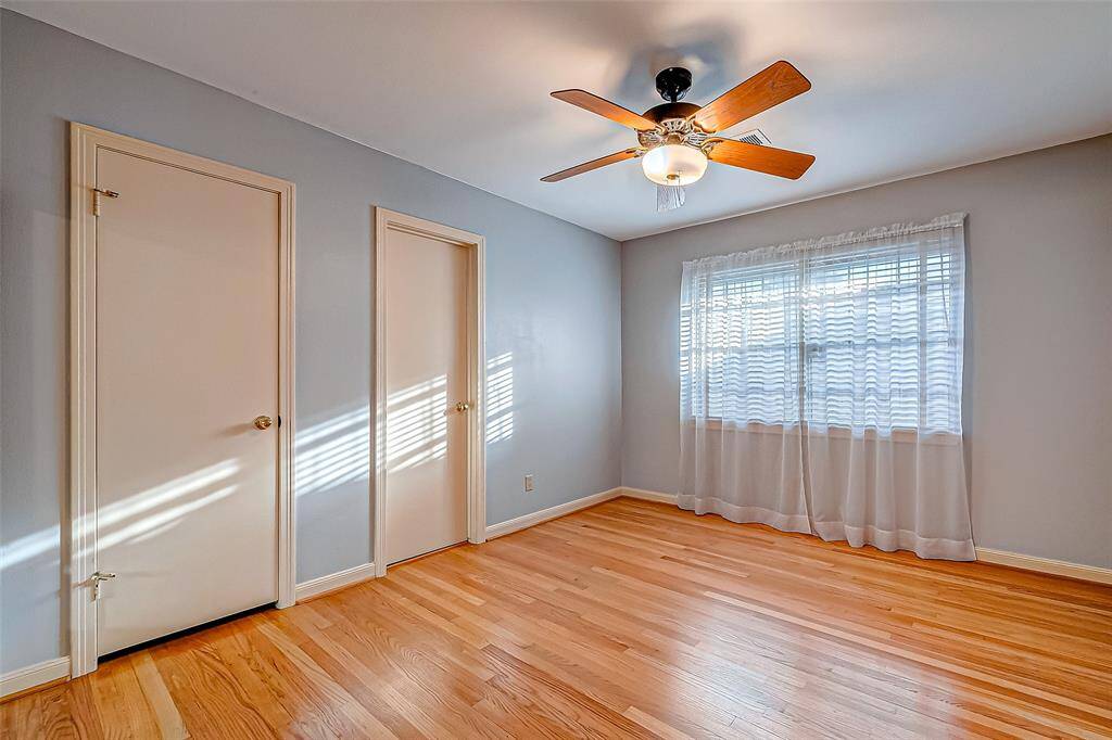 This bright, airy room features polished hardwood floors, a ceiling fan with light, and ample natural light from a large window.