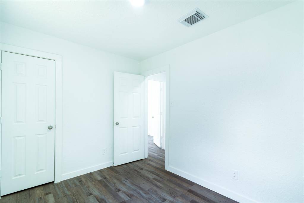 This photo features a modern bathroom with a glass shower enclosure and marble-style tiles. Adjacent is a room with wood flooring and a bright, neutral color scheme, offering a fresh and inviting space.