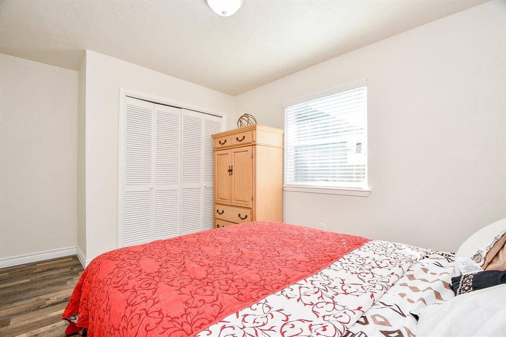 Wonderfully appointed secondary bedroom, featuring neutral paint, laminate wood floors, a large window with privacy blinds, and a built-in closet.