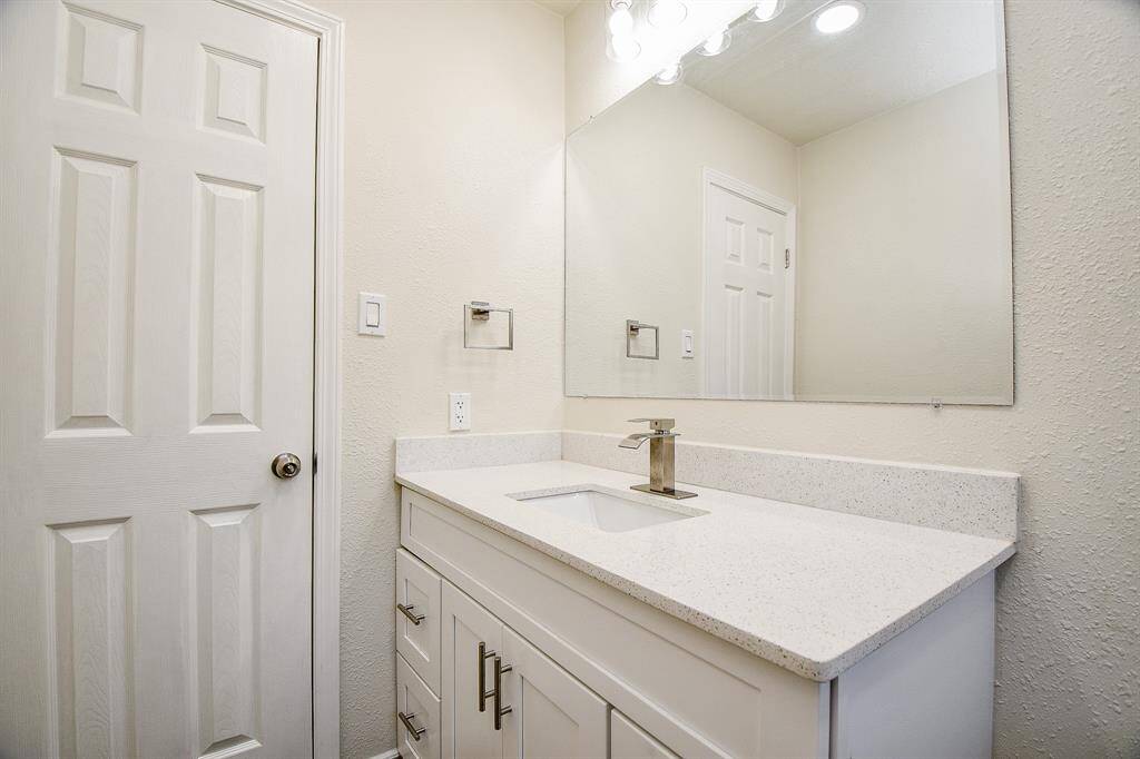 This secondary bathroom has granite countertops and backsplash, a large mirror, and wooden cabinets.