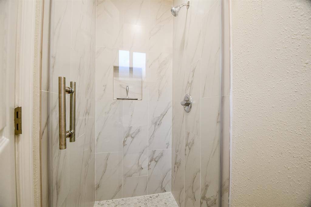 Fully remodeled walk-in shower with gorgeous tile walls, and a glass door.