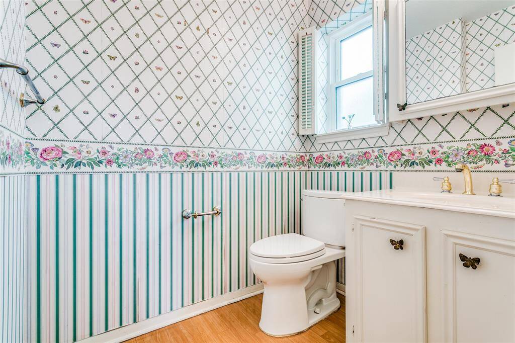 The powder room features a floral and diamond-patterned wallpaper with a coordinating striped lower half, and a white vanity with cabinet storage, Natural light streams in from a small window.