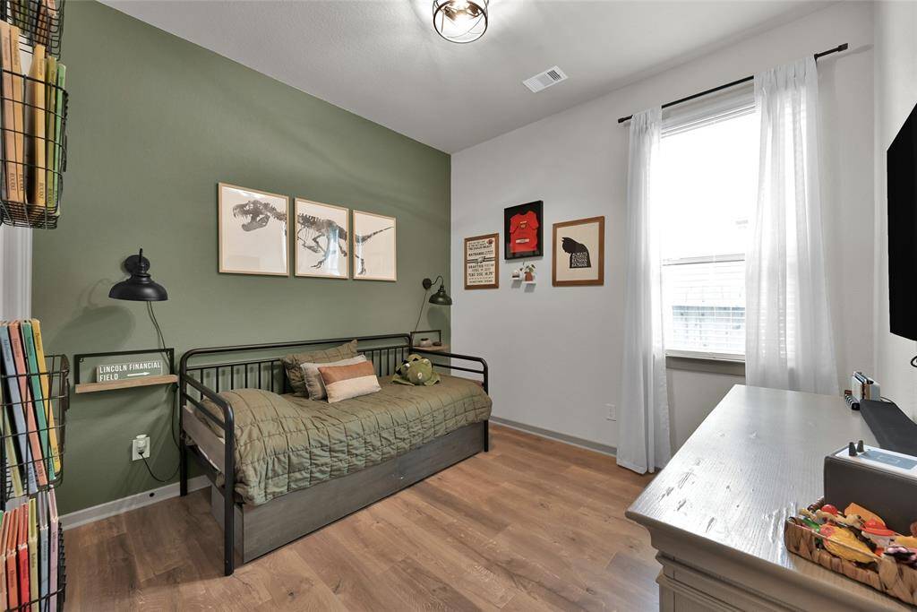 Spacious, well-lit bedroomfeaturing a sage green accent wall.The room has upgraded flooring, alarge window with sheer curtains,and a desk area, creating a cleanand inviting space.
