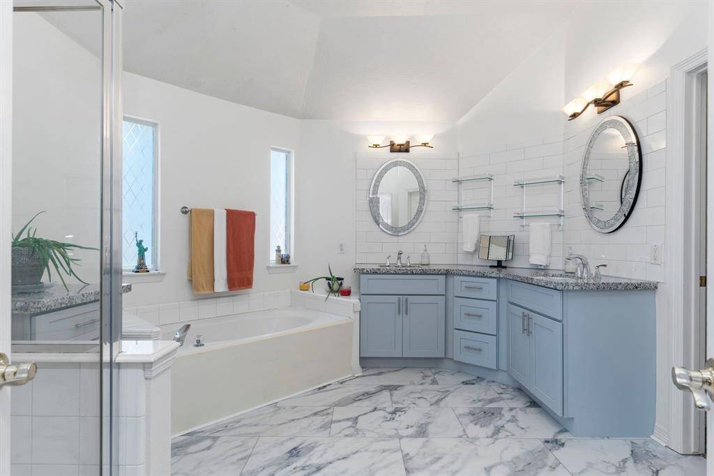 Beautifully renovated primary bath featuring new flooring, chic backsplash, custom shaker vanity, granite countertops, updated mirrors, hardware, and light fixtures. Simply stunning!