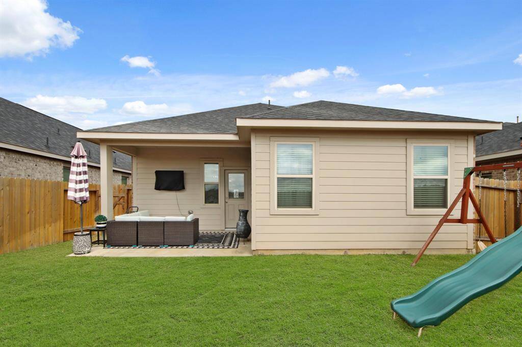This photo shows a cozy backyard with a covered extended patio. The yard features a spacious grassy area, & a wooden fence for privacy, making it great for relaxation and family activities.