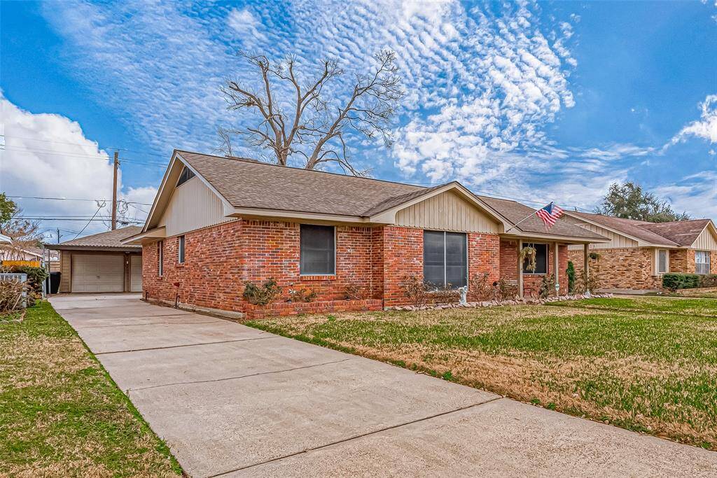 This is a charming single-story brick home featuring a spacious driveway, a well-maintained lawn, and a covered carport.