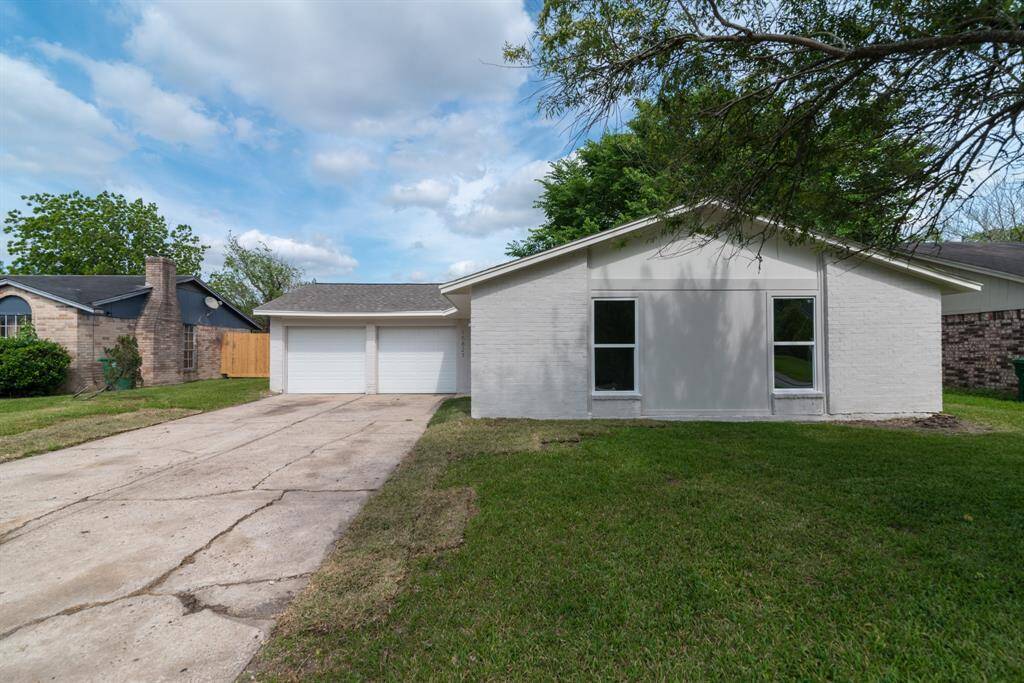 The photo shows a single-story home's backyard with a well-maintained lawn, a large tree providing shade, and a wooden fence for privacy. The house features a light exterior with double glass doors and a small concrete patio area.