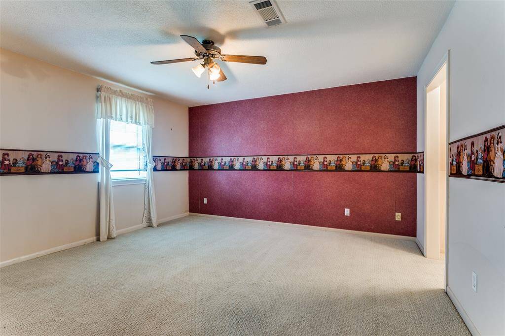 This spacious second bedroom with a two-tone color scheme, featuring light carpet and a ceiling fan with lighting. The room includes a window, custom built in shelves and drawers, large walk in closet and decorative border. There is a Jack and Jill bathroom.