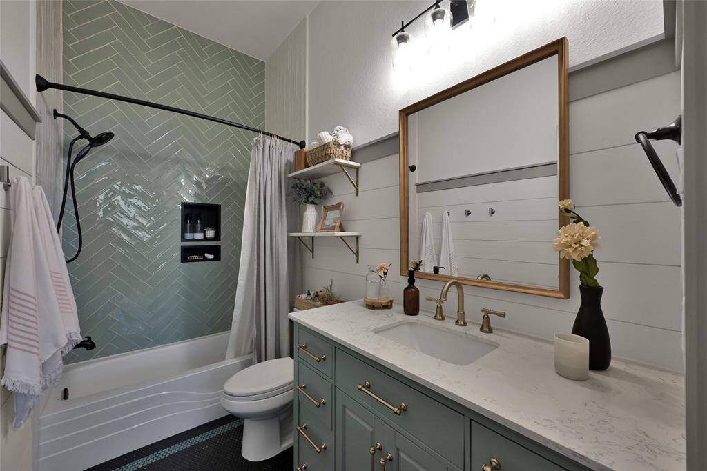 A modernbathroom with stylish herringbonetile in the shower, a sleek whitebathtub, and vanity with brasshardware. It also features a largemirror with a wooden frame,shiplap walls, and contemporarylighting fixtures.